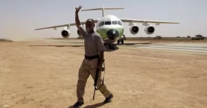 En la imagen se ve el aeropuerto de Sirte, construido aprovechando la carretera como pista, un avión que para llegar a la 'terminal' tiene que rodar sobre la arena del desierto y a un libio ataviado con el 'traje regional'.