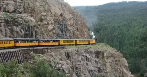 Un ferrocarril de vía estrecha se desplaza por una zona montañosa. Los ferrocarriles de vía estrecha permiten la construcción con radios de curva pequeños y vías con estructuras más pequeñas, siendo por tanto sustancialmente más económicos de construir, equipar y operar que los ferrocarriles de vía de ancho estándar, por lo que son ampliamente utilizados en terrenos montañosos.